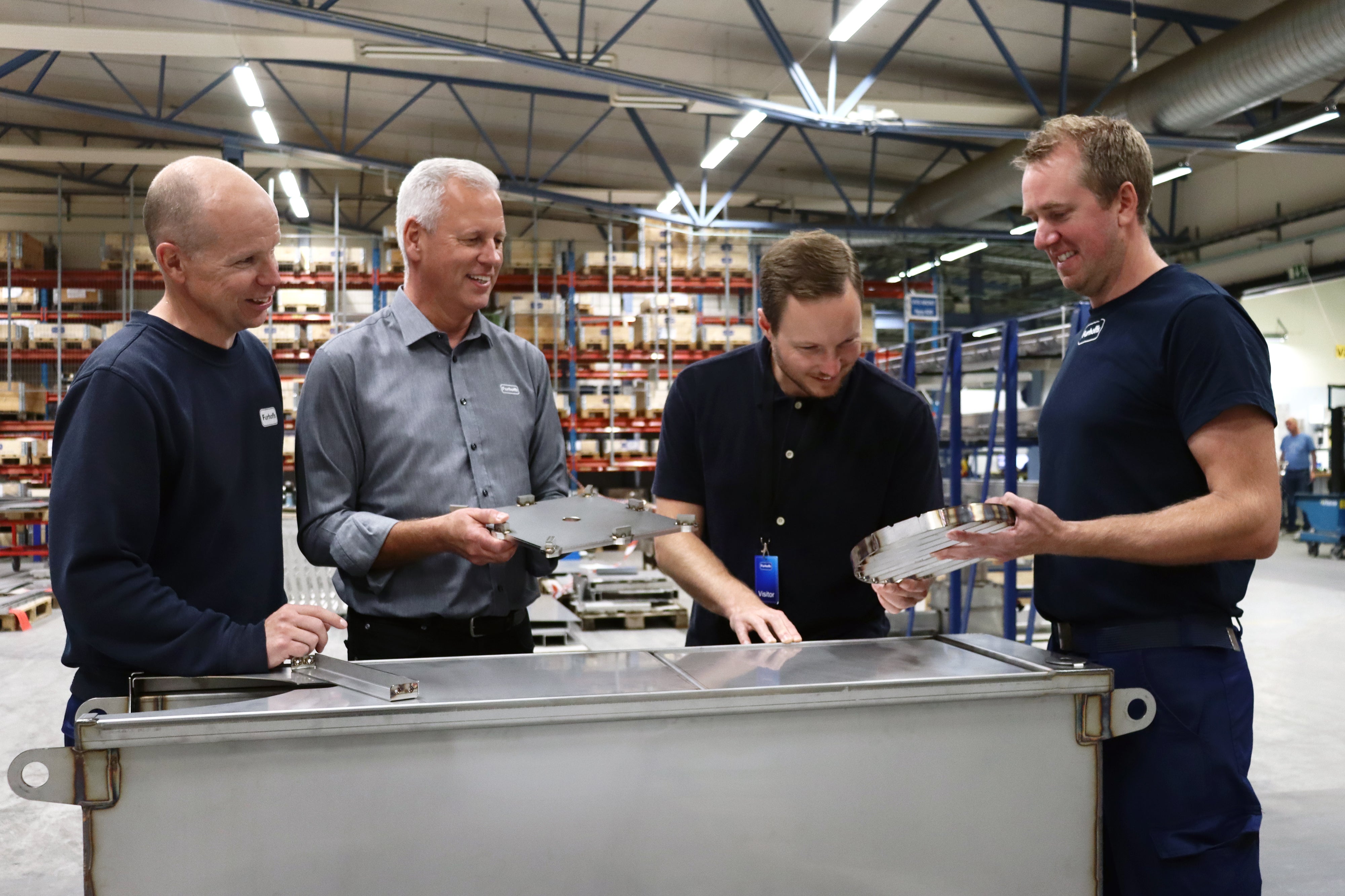 Medarbetare och kund granskar rostfria produkter tillsammans i Furhoffs industrimiljö – Legoproduktion i rostfritt stål.